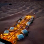 Aerial view of a luxury Sahara desert camp illuminated with warm lanterns at night during a 3 days desert tour from Fes to Marrakech.