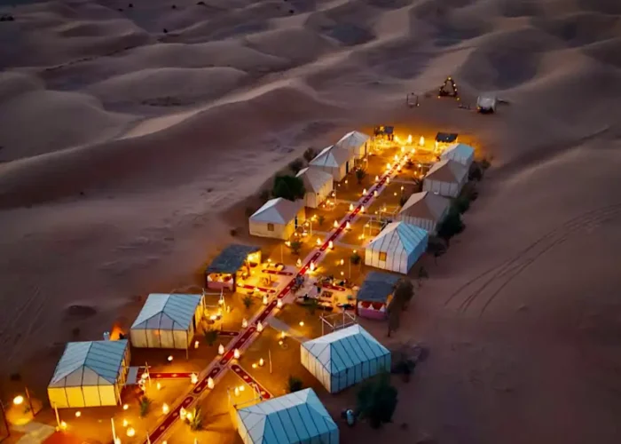 Aerial view of a luxury Sahara desert camp illuminated with warm lanterns at night during a 3 days desert tour from Fes to Marrakech.